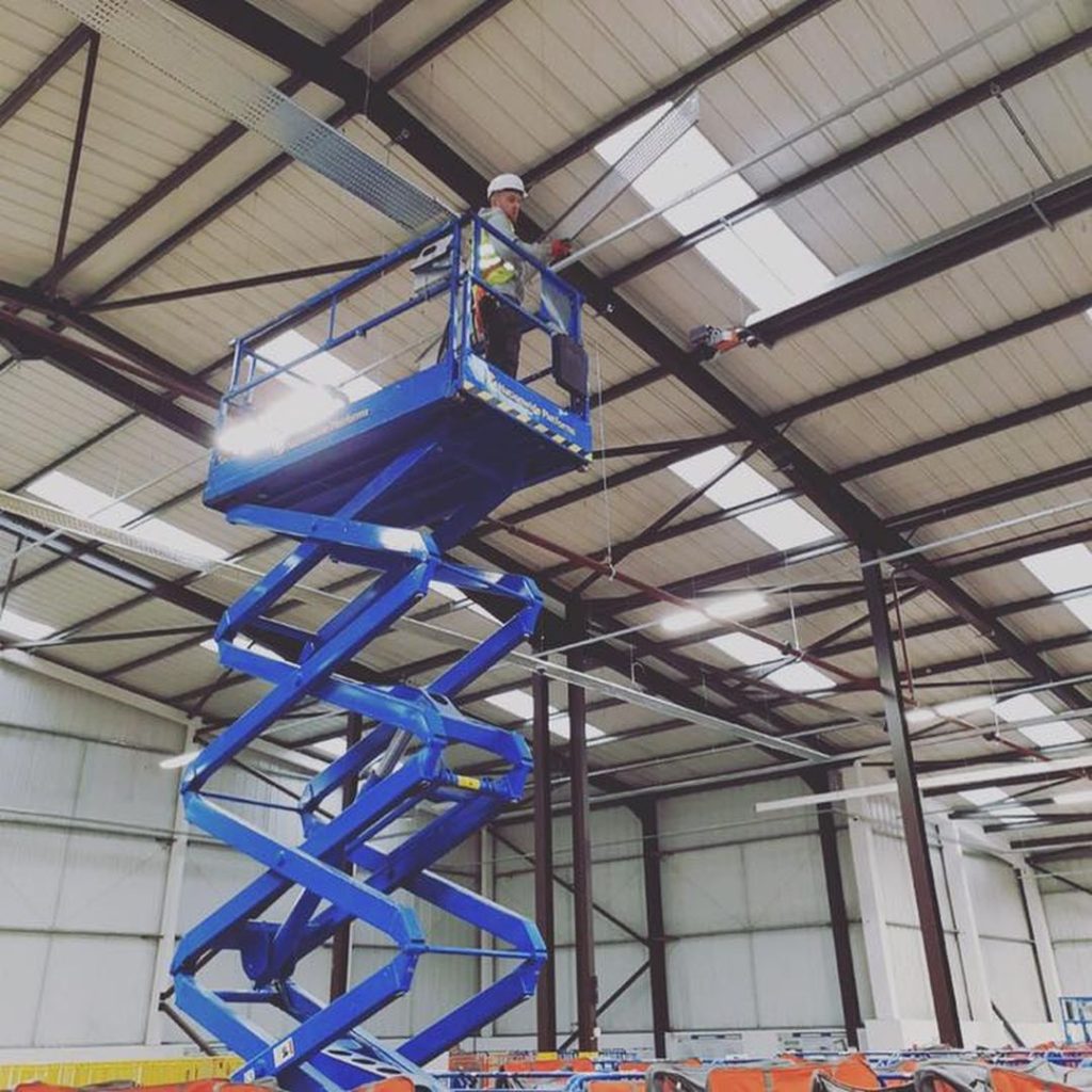 electrician on cherry picker changing bulbs in warehouse